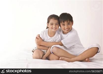 Portrait of happy brother embracing sister in bed