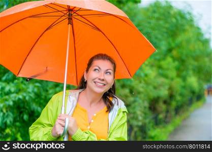 portrait of happy brunette wearing a raincoat under an orange umbrella in the rain