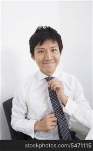 Portrait of happy businessman adjusting necktie at office