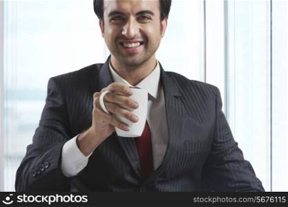 Portrait of happy businessman drinking coffee in office