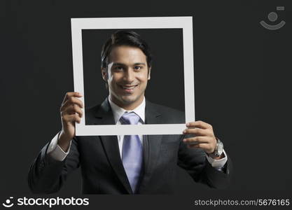 Portrait of happy businessman holding picture frame over black background