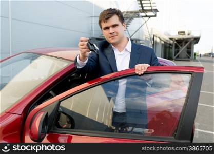 Portrait of happy businessman posing at new car with keys