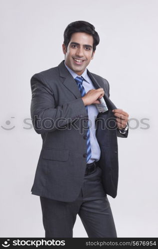 Portrait of happy businessman putting money in pocket over gray background