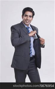 Portrait of happy businessman putting money in pocket over gray background