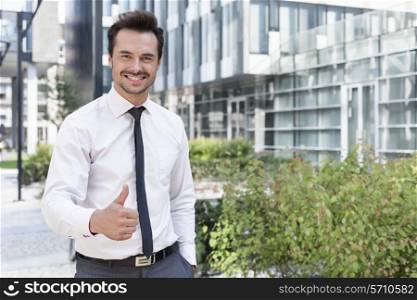 Portrait of happy businessman showing thumbs up outside office building