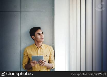 Portrait of Happy Businessman Standing by the Window in Office. Using Digital Tablet. Looking Away and Smiling. Dreaming for Success