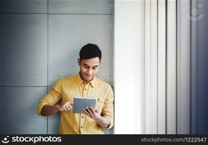 Portrait of Happy Businessman Standing by the Window in Office. Using Digital Tablet and Smiling