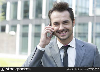 Portrait of happy businessman using cell phone outside office