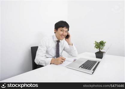 Portrait of happy businessman using cell phone while working at office desk