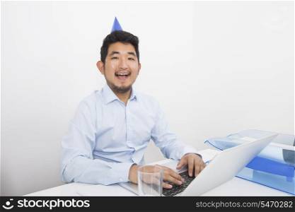 Portrait of happy businessman wearing party hat while working in office