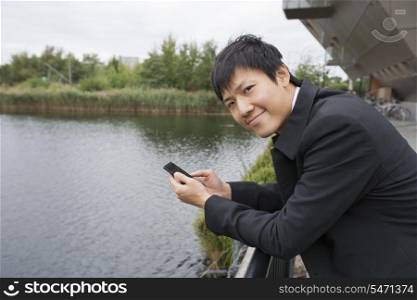 Portrait of happy businessman with cell phone leaning on bridge railing