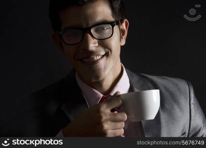 Portrait of happy businessman with coffee cup against black background