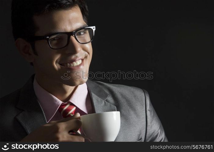 Portrait of happy businessman with coffee cup against black background