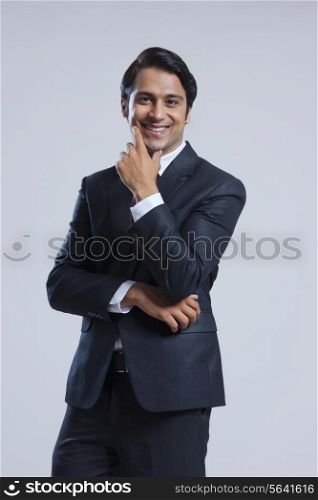 Portrait of happy businessman with hand on chin over gray background