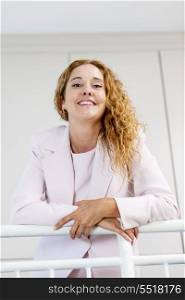 Portrait of happy businesswoman in office. Smiling proud business woman standing in office hallway leaning on railing shot from below
