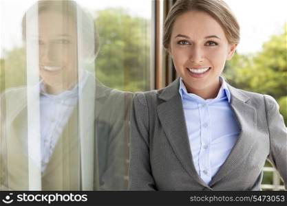Portrait of happy businesswoman leaning on glass door