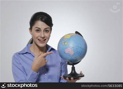 Portrait of happy businesswoman pointing at globe against gray background
