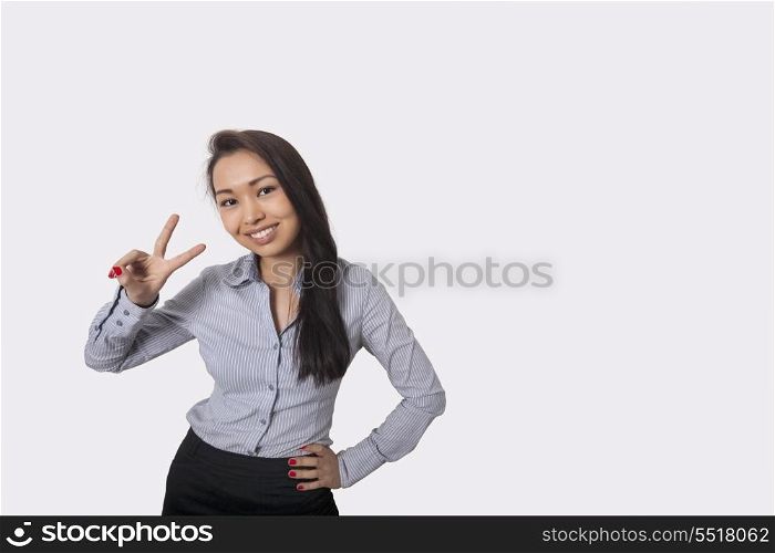 Portrait of happy businesswoman showing victory sign against gray background