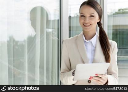 Portrait of happy businesswoman using digital tablet by glass door