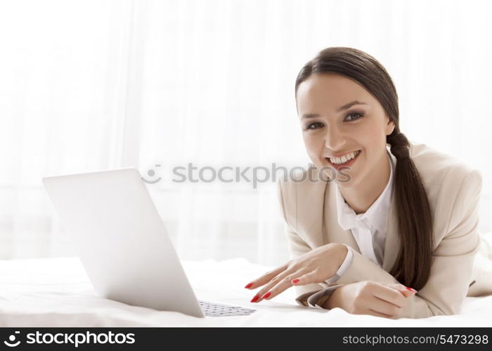 Portrait of happy businesswoman using laptop in hotel room