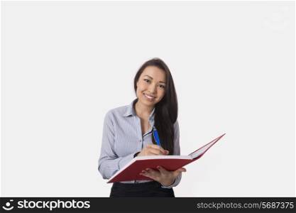 Portrait of happy businesswoman with book and pen over white background