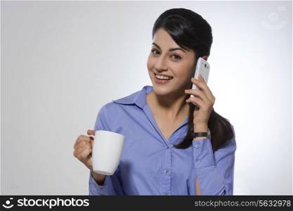 Portrait of happy businesswoman with coffee mug using phone against gray background