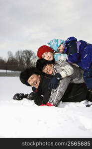 Portrait of happy Caucasian family of four lying stacked on top of each other in snow smiling at viewer.