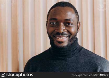 Portrait of happy cheerful african american man smiling at camera, expressing positive emotions. Headshot of handsome dark-skinned guy in grey poloneck sweater posing for indoor photo,. Portrait of happy cheerful african american man smiling at camera, expressing positive emotions