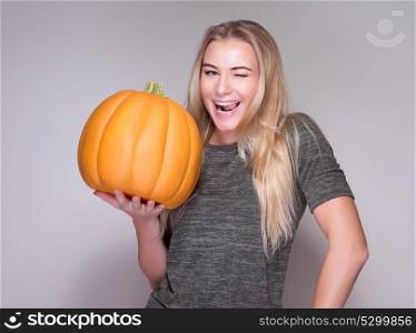 Portrait of happy cheerful woman holding in hand big orange pumpkin isolated on gray background, Thanksgiving day celebration