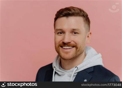 Portrait of happy cheerful young man with beard wearing stylish casual clothes smiling at camera while standing isolated on pink background. Handsome red haired guy with positive face expression. Young cheerful handsome man on pink background