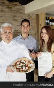 Portrait of happy chef holding pizza with young couple
