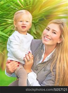 Portrait of happy cute mother with little baby in tropical park in sunny day, having fun outdoors, healthy lifestyle, love and childcare concept
