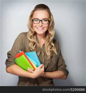 Portrait of happy cute student girl with books in hands over gray background, enjoying first days of education in high school