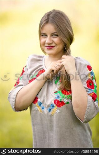Portrait of happy cute woman in traditional ukrainian clothes making braid at field