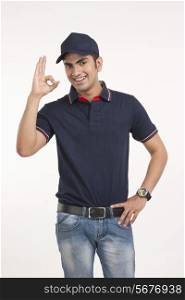 Portrait of happy delivery man gesturing OK sign against white background
