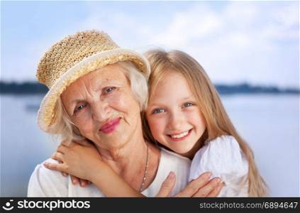 Portrait of Happy Embracing Grandmother and Granddaughter looking at the Camera at the Sunny Summer Day