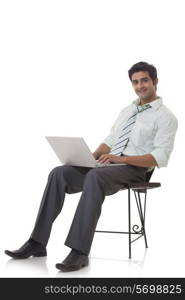 Portrait of happy executive on chair using laptop