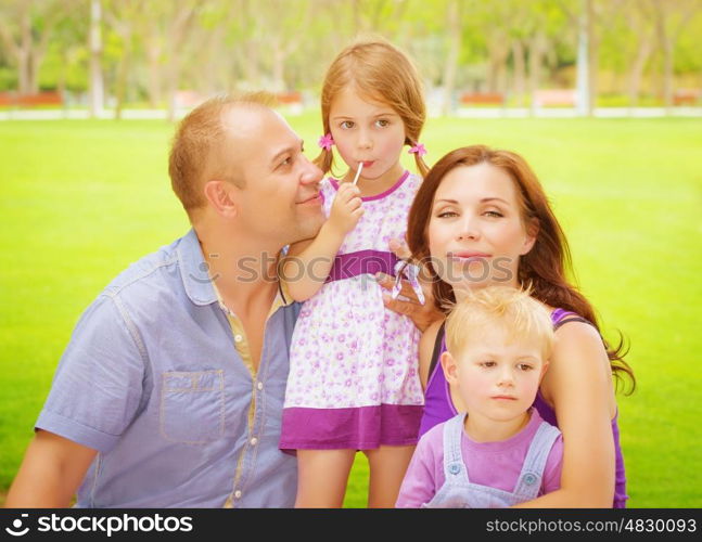 Portrait of happy family having fun outdoors, young parents with two cute kids in spring park, spending time together, love concept