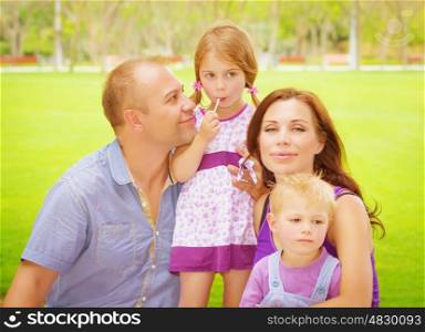 Portrait of happy family having fun outdoors, young parents with two cute kids in spring park, spending time together, love concept