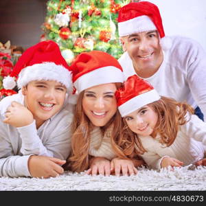 Portrait of happy family in Christmas eve at home, cheerful parents with two cute kids lying down on the floor near beautiful decorated Xmas tree&#xA;