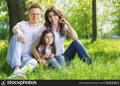 Portrait of happy family in park. Portrait of happy family sitting on grass under a tree in park on a sunny day