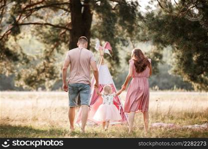 Portrait of happy family. Mom, dad and daughter walk in the park in nature. Young family spending time together on vacation, outdoors. The concept of summer holiday. Mother&rsquo;s, father&rsquo;s, baby&rsquo;s day.. Portrait of happy family. Mom, dad and daughter walk in the park in nature. Young family spending time together on vacation, outdoors. The concept of summer holiday. Mother&rsquo;s, father&rsquo;s, baby&rsquo;s day