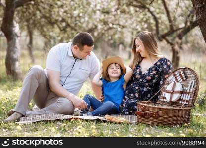 Portrait of happy family on picnic. pregnant Mom, dad and daughter sitting in spring blooming park. Young family spending time together on vacation, outdoors. Portrait of happy family on picnic. pregnant Mom, dad and daughter sitting in spring blooming park. Young family spending time together on vacation, outdoors.