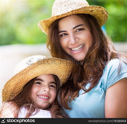 Portrait of happy family outdoors, cute cheerful mother with little daughter wearing identical straw hats and having fun on backyard