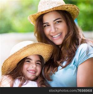 Portrait of happy family outdoors, cute cheerful mother with little daughter wearing identical straw hats and having fun on backyard