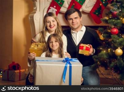 Portrait of happy family posing with Christmas gifts at fireplace