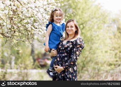 Portrait of happy family. pregnant mom and little daughter walk in spring blooming park. Young family spending time together on vacation, outdoors. The concept of holiday. Mother’s, baby’s day. Portrait of happy family. pregnant mom and little daughter walk in spring blooming park. Young family spending time together on vacation, outdoors. The concept of holiday. Mother’s, baby’s day.