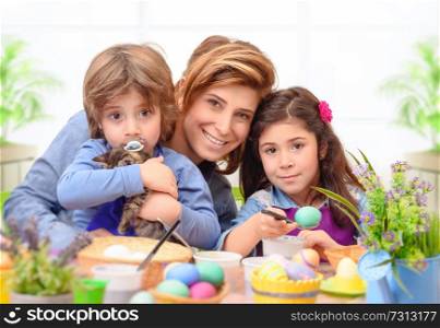 Portrait of happy family preparing to Easter, mother with two cute kids dyeing eggs, traditional Easter symbol, having fun together at home