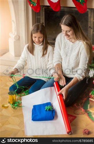 Portrait of happy family wrapping Christmas presents at fireplace