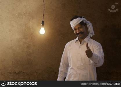 Portrait of happy farmer showing thumb up while standing against light bulb